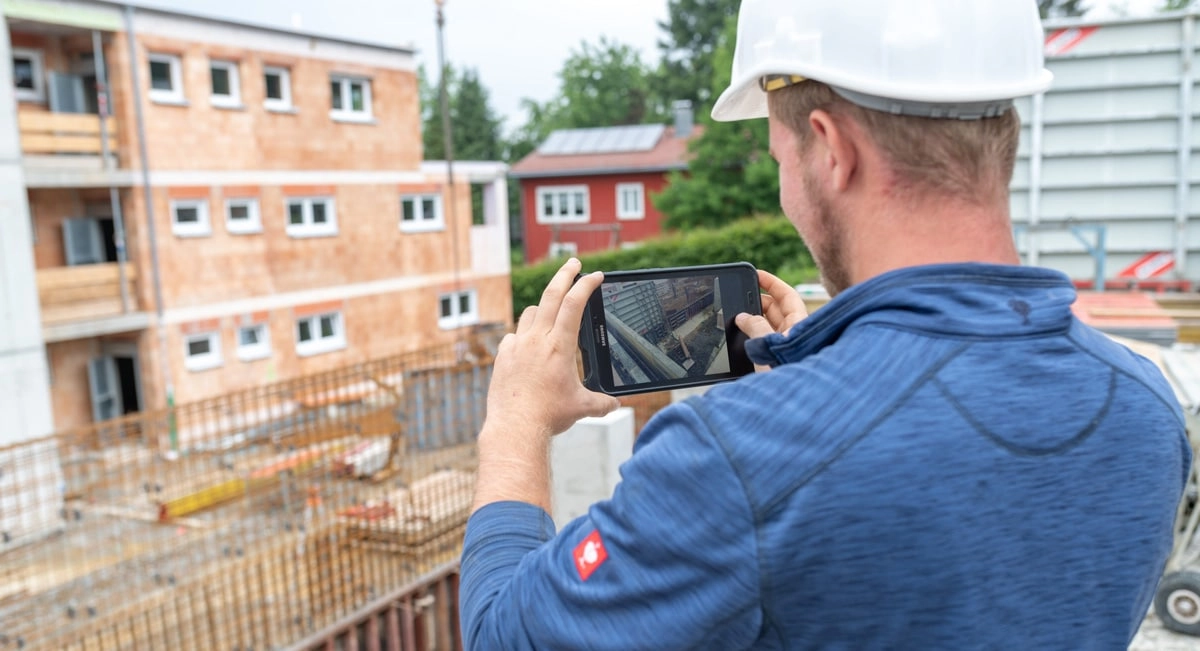 Ein Bauarbeiter fotografiert mithilfe seines Handys den Fortschritt auf einer Baustelle
