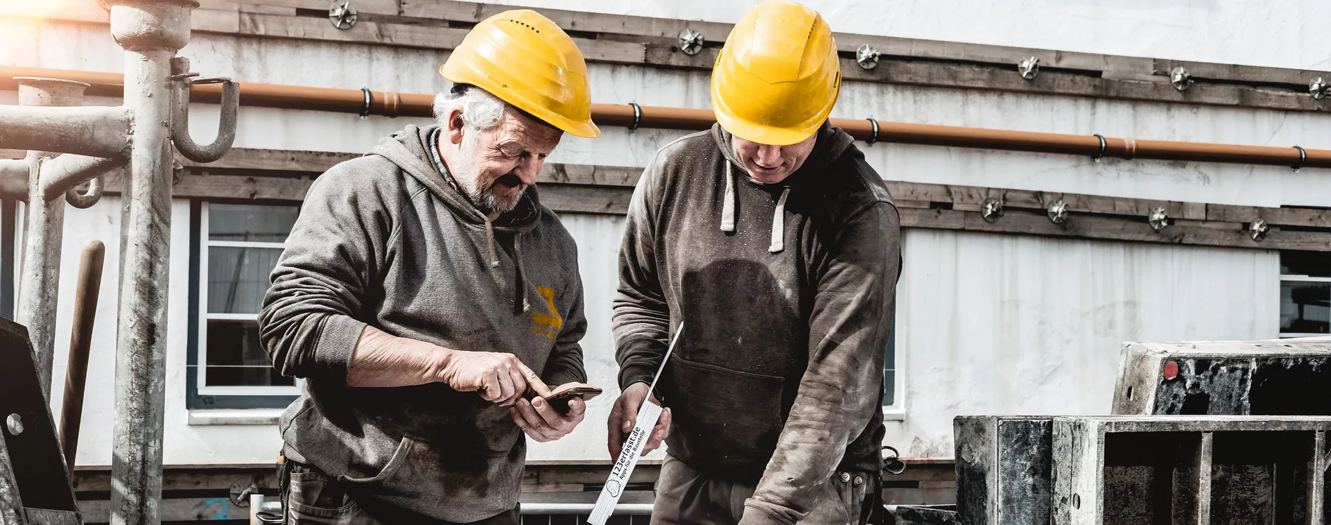 Zwei Bauarbeiter der Edlef Jensen GmbH auf der Baustelle, mit einem Handy in der Hand