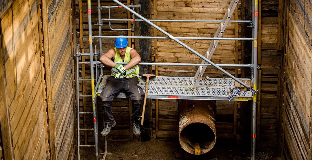Bauarbeiter sitzt mit den Armen über dem Geländer auf einem Baustellen-Gerüst