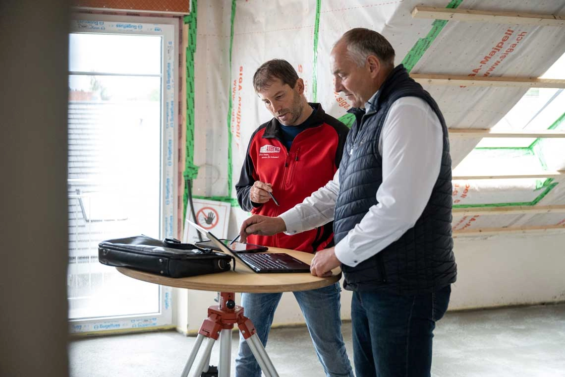 Dipl.-Ing. Norbert Kees der Amberg Bau GmbH und ein weiterer Mitarbeiter gehen auf der Baustelle die digitalen Baupläne durch